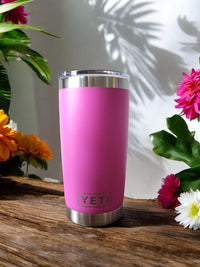 a pink yeti cup sitting on a wooden table next to flowers